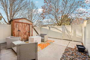 Fenced backyard with a gate, a storage shed, and a patio area