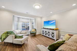 Living room featuring light wood-style flooring, a textured ceiling, recessed lighting, and ornamental molding