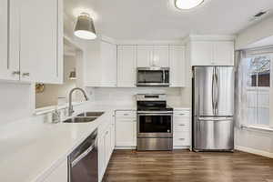Kitchen with appliances with stainless steel finishes, white cabinets, dark wood-style flooring, a textured ceiling, and light stone counters
