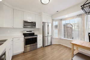 Kitchen featuring stainless steel appliances, white cabinetry, light wood finished floors, and light stone counters