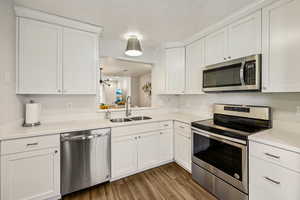 Kitchen with stainless steel appliances, white cabinets, and dark wood-style floors