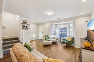 Living room featuring light wood-type flooring, stairs, crown molding, a textured ceiling, and recessed lighting