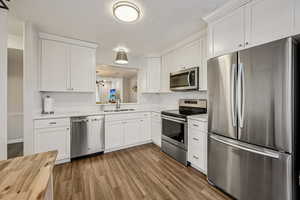 Kitchen featuring appliances with stainless steel finishes, white cabinets, dark wood finished floors, a textured ceiling, and wood counters