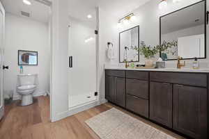 Bathroom with a shower stall, double vanity, light wood-style flooring, and recessed lighting