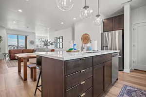 Kitchen featuring dark brown cabinets, open floor plan, a kitchen bar, a kitchen island with sink, and recessed lighting