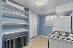 Kitchen featuring radiator, white appliances, a textured ceiling, and light tile patterned floors