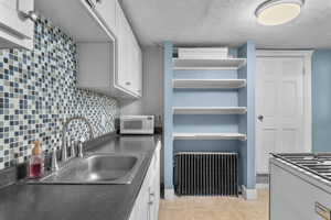 Kitchen featuring radiator heating unit, white cabinetry, backsplash, a textured ceiling, and white microwave
