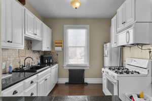 Kitchen with white appliances, white cabinets, radiator, dark wood finished floors, and backsplash