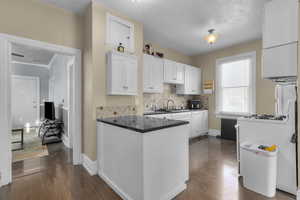 Kitchen with white cabinetry, a peninsula, white appliances, backsplash, and dark wood-style flooring