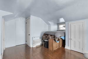Bedroom featuring wood finished floors, radiator heating unit, vaulted ceiling, and a textured ceiling