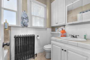 Bathroom featuring radiator heating unit, wainscoting, vanity, light tile patterned floors, and wood walls