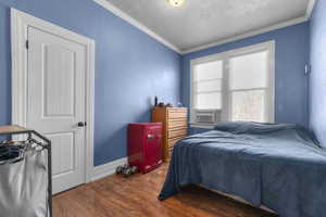 Bedroom with wood finished floors, crown molding, a textured ceiling, and cooling unit