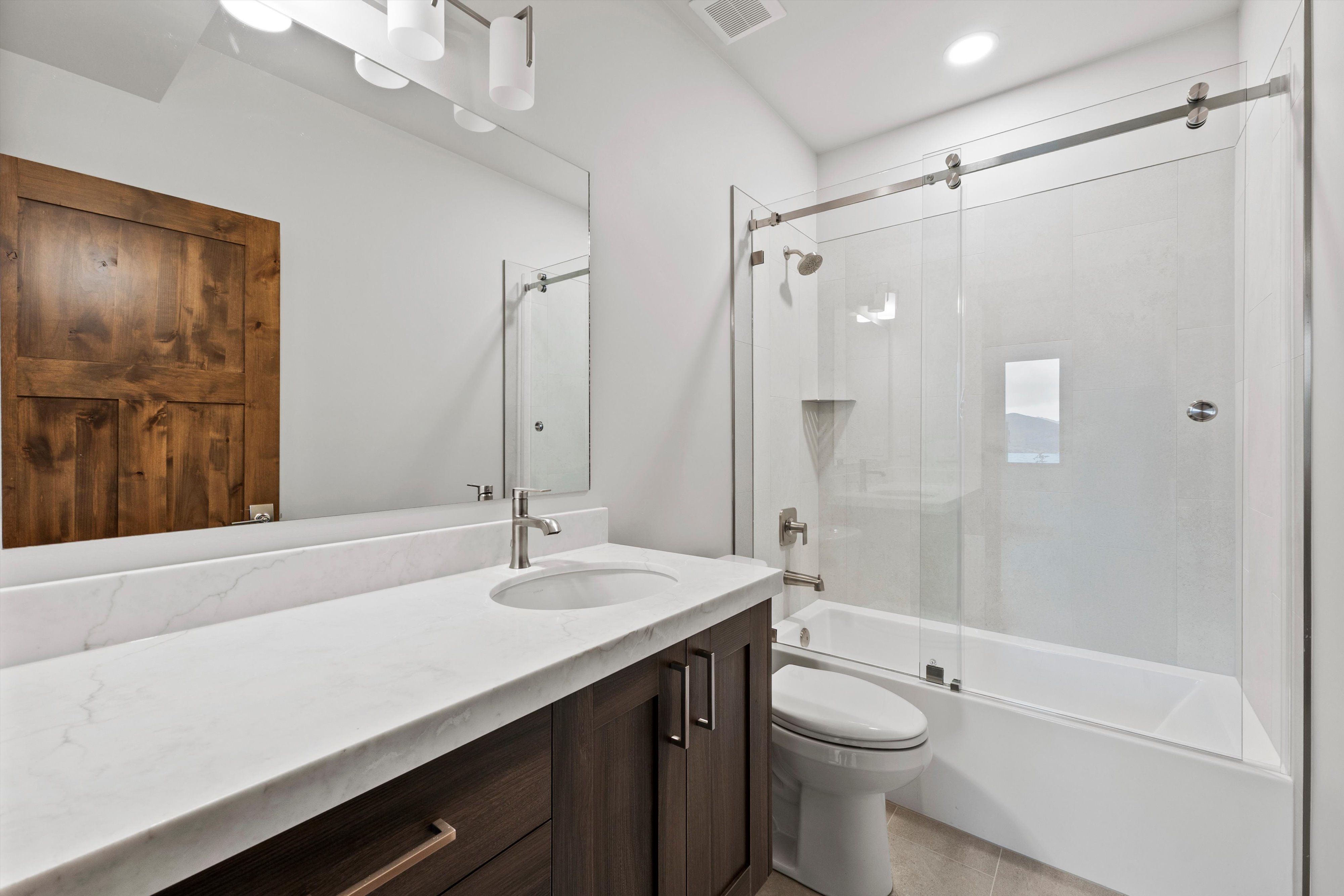 Bathroom featuring a single vanity with a white countertop and undermount sink, dark wood-finish cabinetry, and a full-width mirror