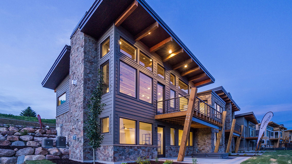 Back of house at dusk with stone siding, a balcony, and a patio area