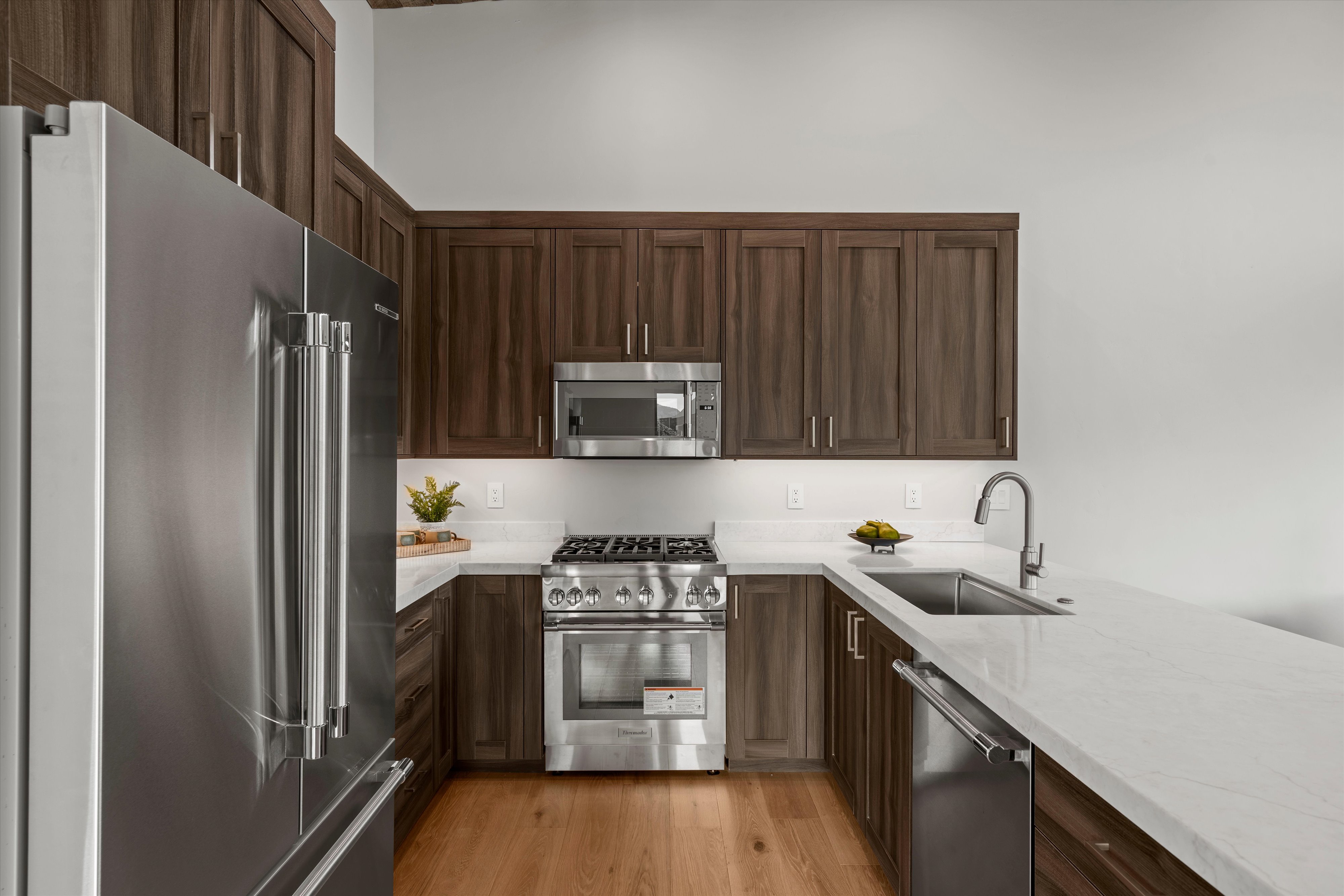 U-shaped kitchen featuring wood cabinetry, stainless steel appliances, white countertops, and wood-finish flooring