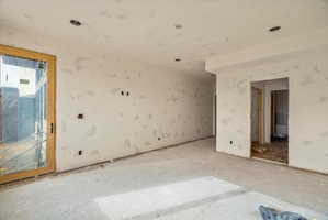 Interior space showcasing a large glass door with a light wood frame, multiple recessed light fixtures, and raw drywall finishes