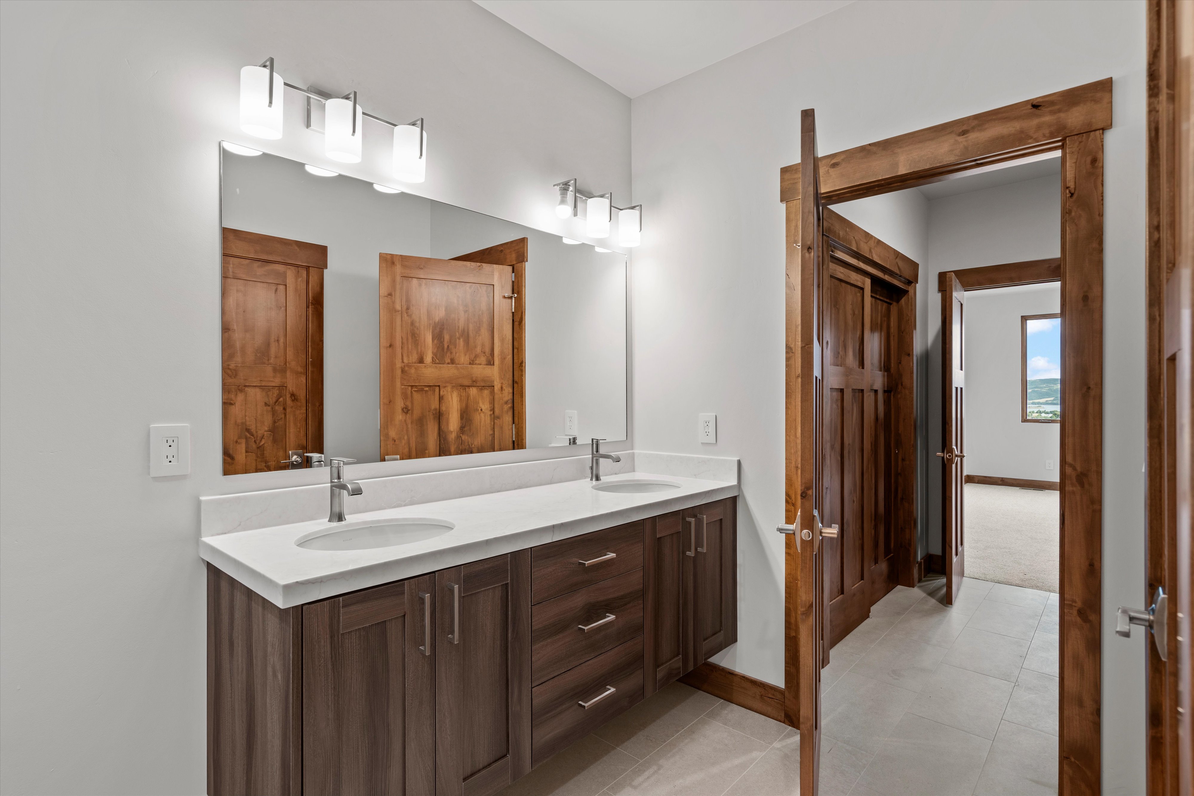 Double vanity with a light-toned countertop, dual undermount sinks, and contemporary wall-mounted light fixtures