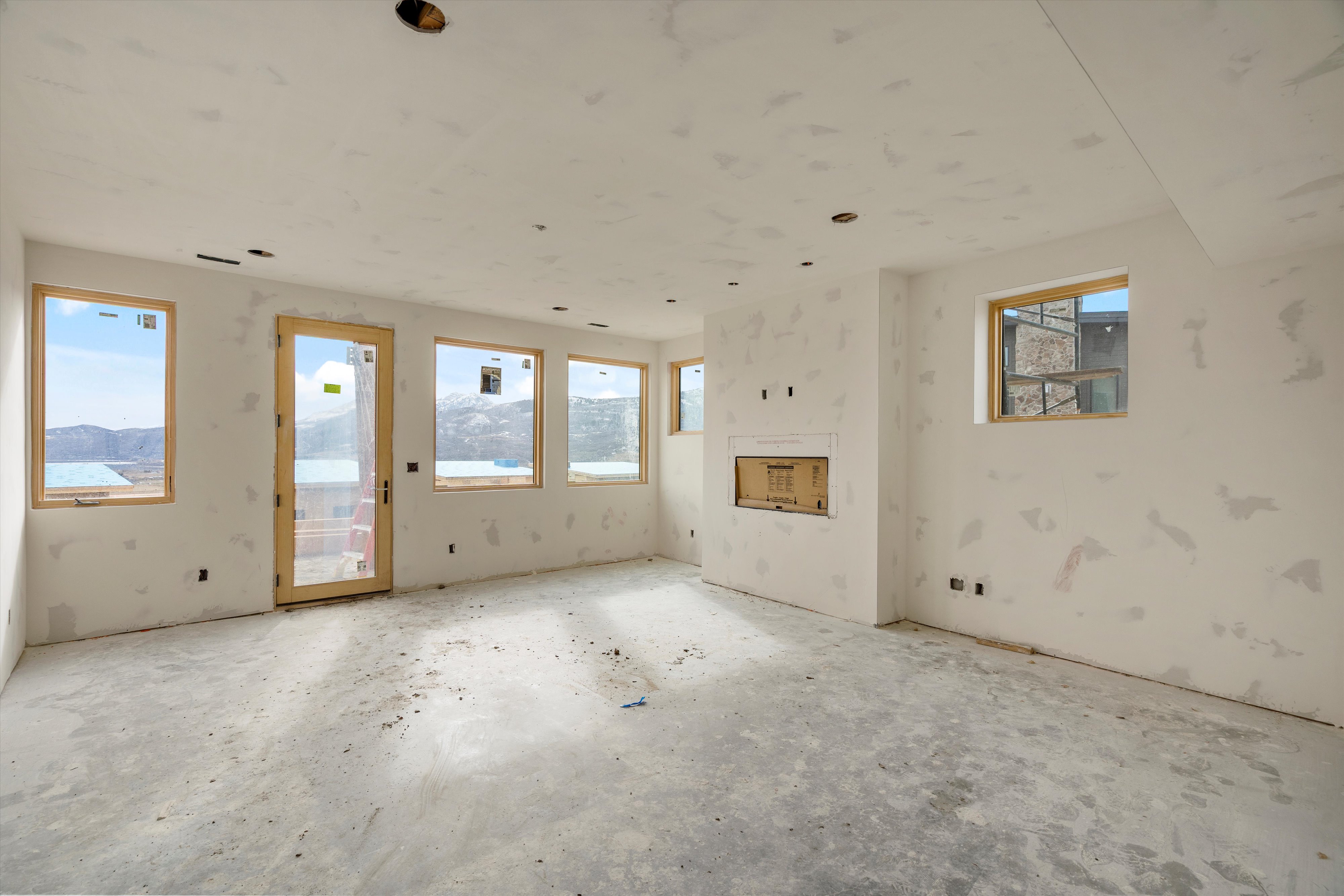 Spacious room under construction featuring multiple windows, a glass-paneled door, and a built-in fireplace opening