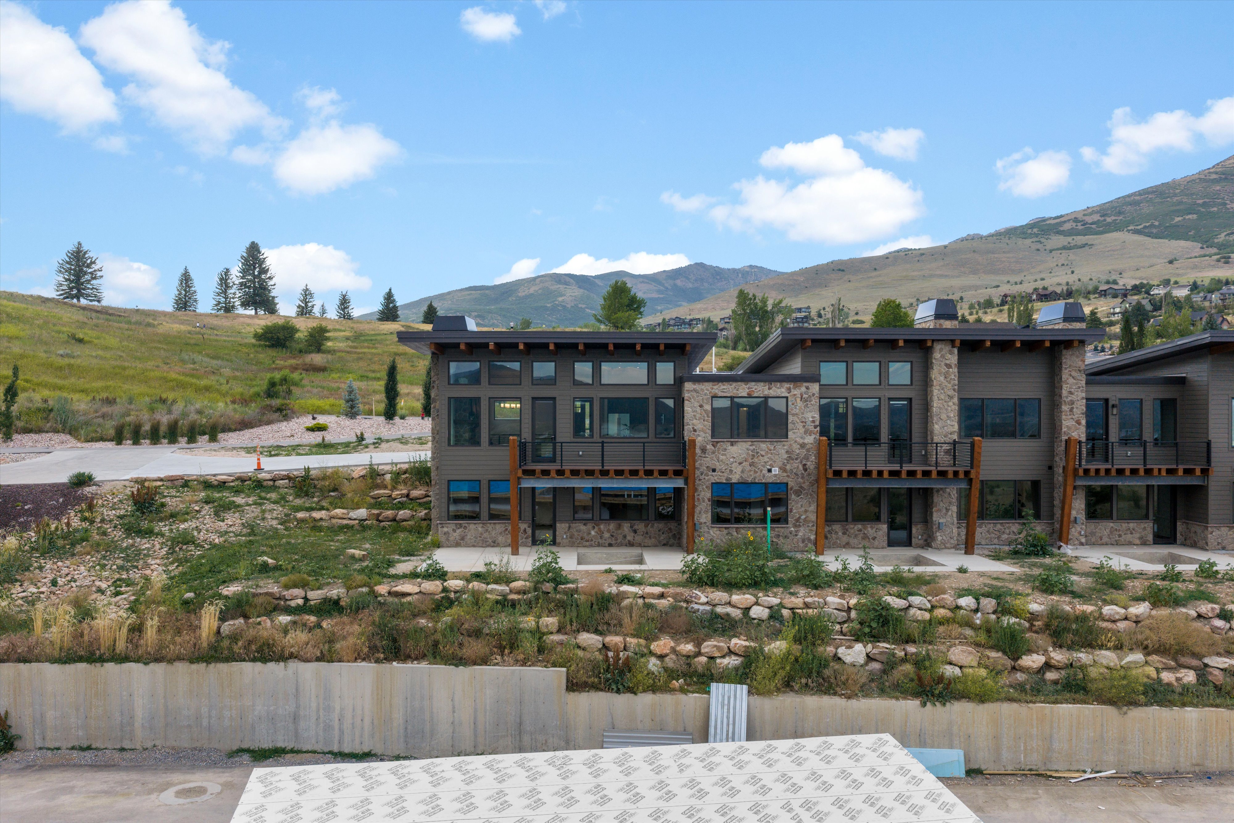 Contemporary multi-story exterior featuring stone and horizontal siding, extensive window arrangements, multiple private balconies, and a distinctive flat roofline
