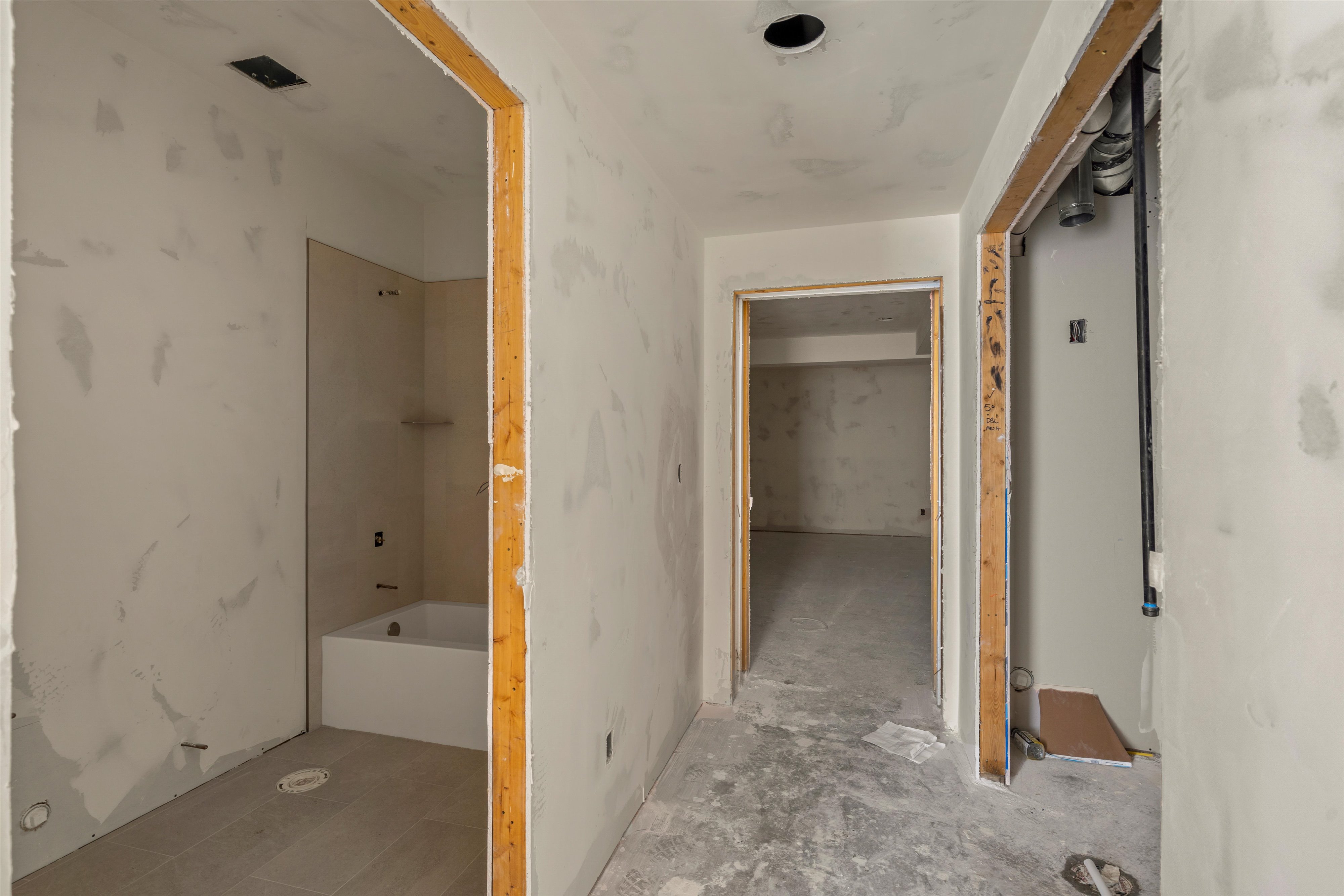 Interior hallway with exposed wood door frames, unfinished drywall, a recessed ceiling light, and concrete flooring