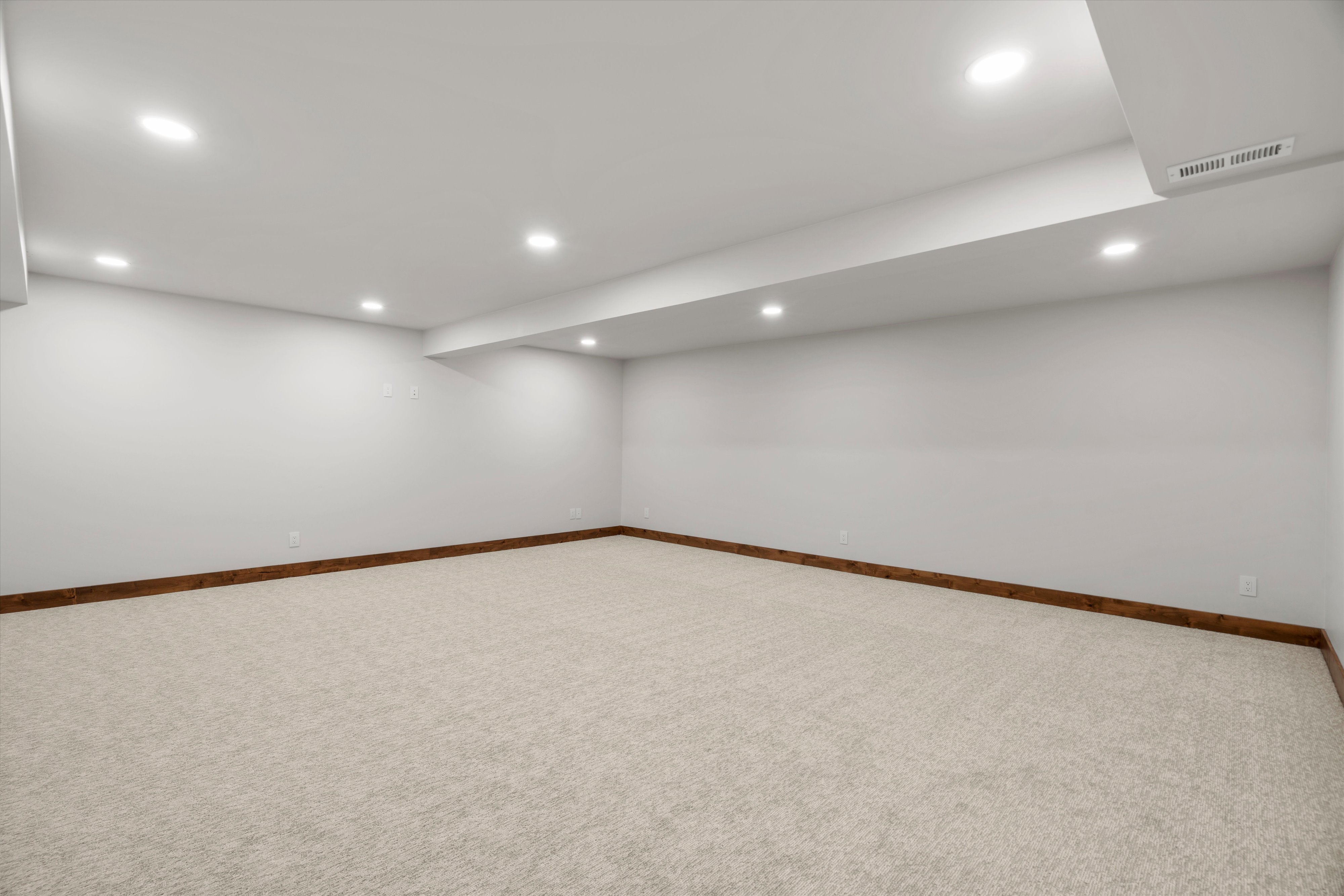 Spacious room featuring neutral carpeting, light-toned walls, recessed ceiling lighting, and dark wood trim