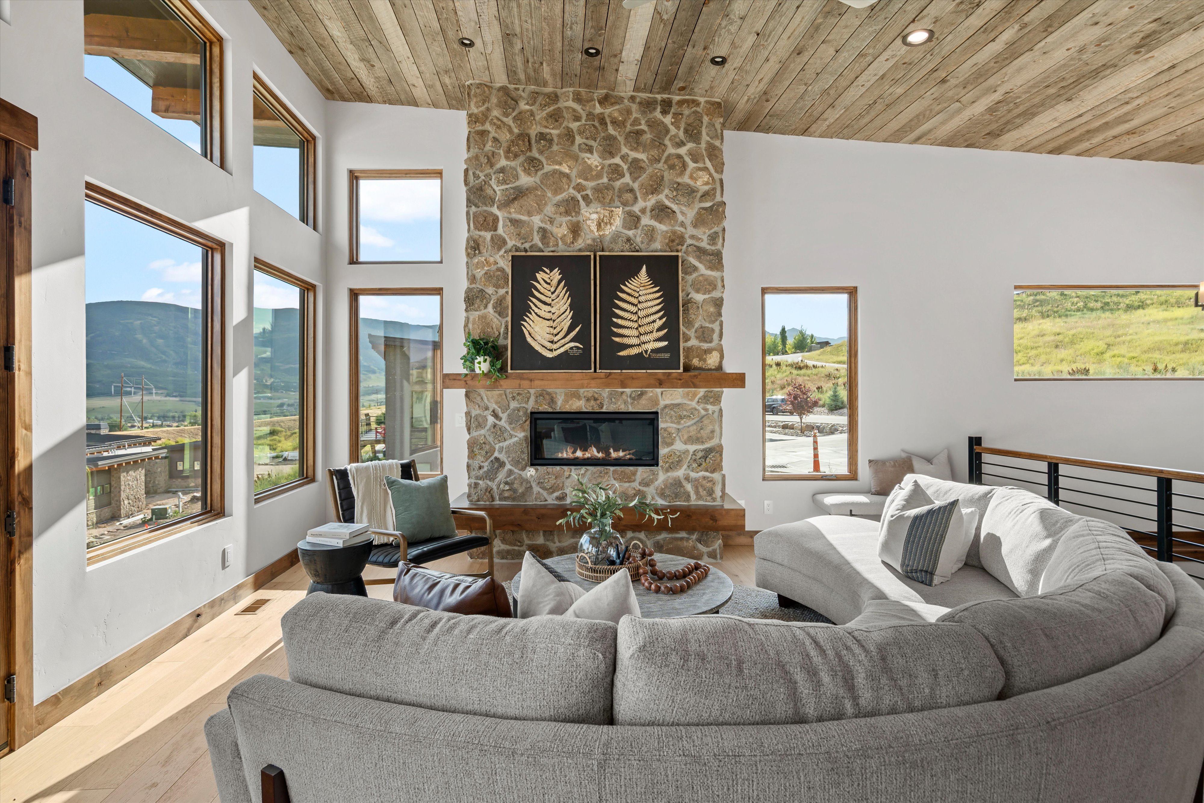 Living space featuring a prominent stone-clad fireplace with a wood mantel, wood-finish flooring, and a natural wood plank ceiling