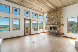 Spacious room featuring a floor-to-ceiling stone fireplace with a wood mantle and electric insert, multiple large windows with wood trim, and a wood-finish ceiling