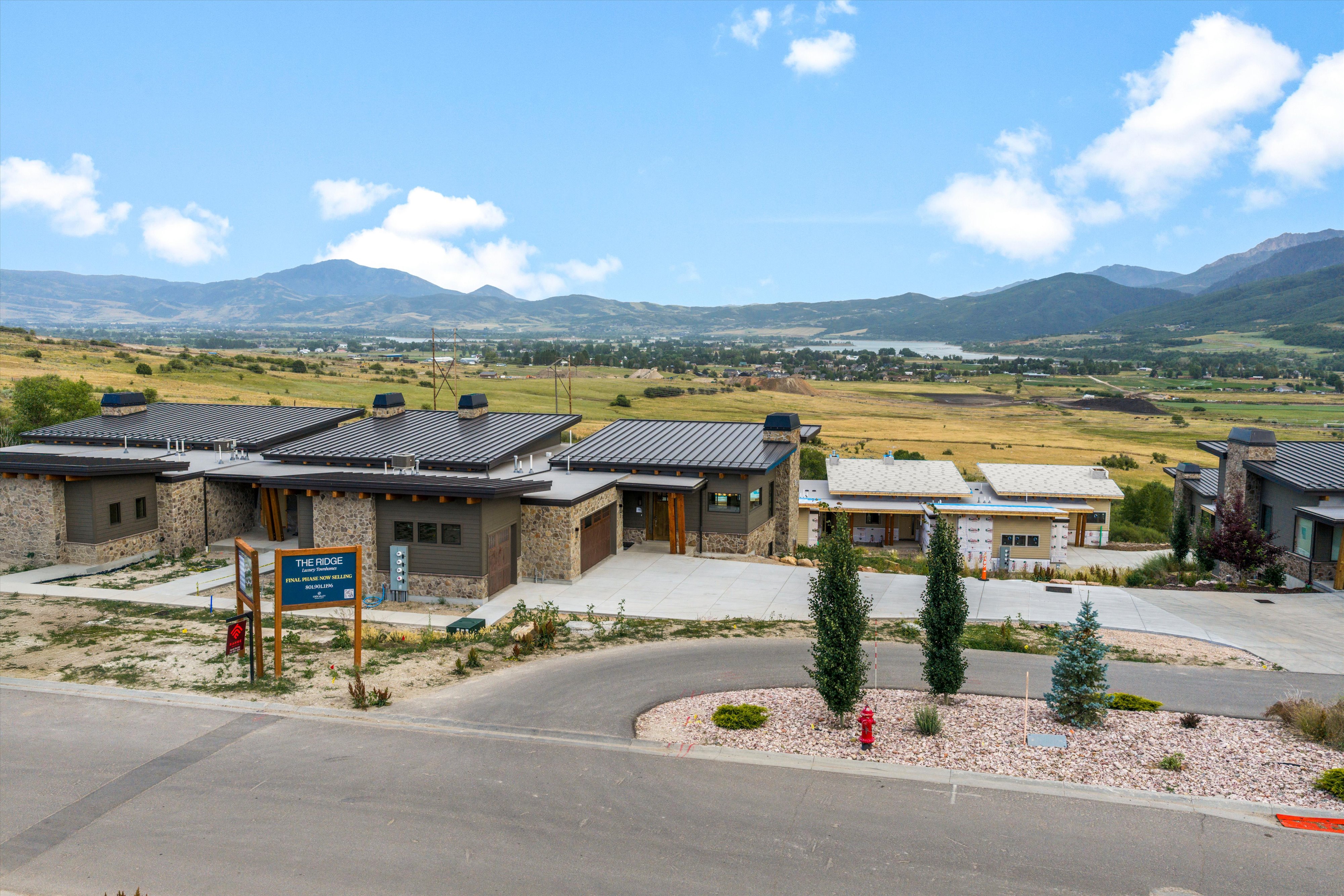 Contemporary mountain-style architecture featuring stone and panel siding, dark metal roofs, and attached garages