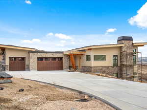 View of front of house featuring stone siding, concrete driveway, a garage, and a chimney