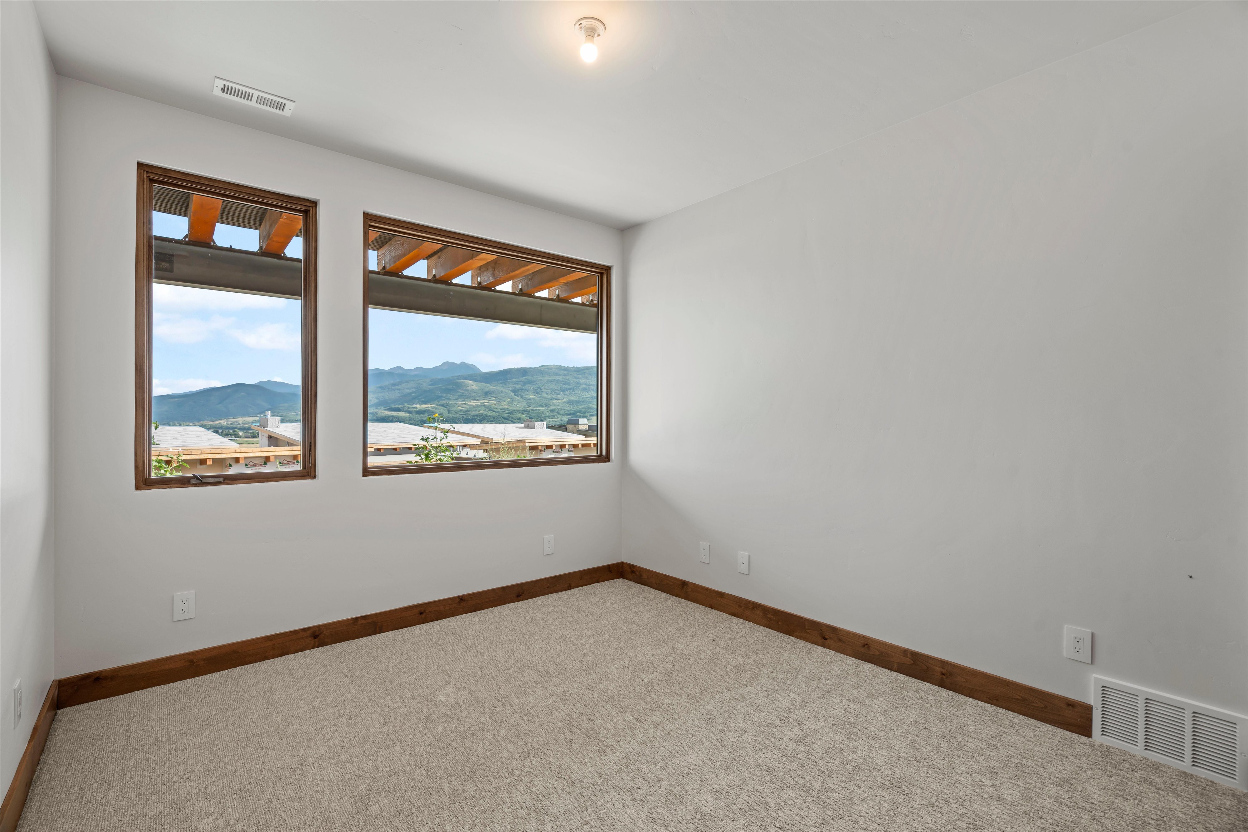 Bright room featuring two large windows with wood trim, neutral carpeting, white painted walls, wood-finish baseboards, and a ceiling-mounted light fixture