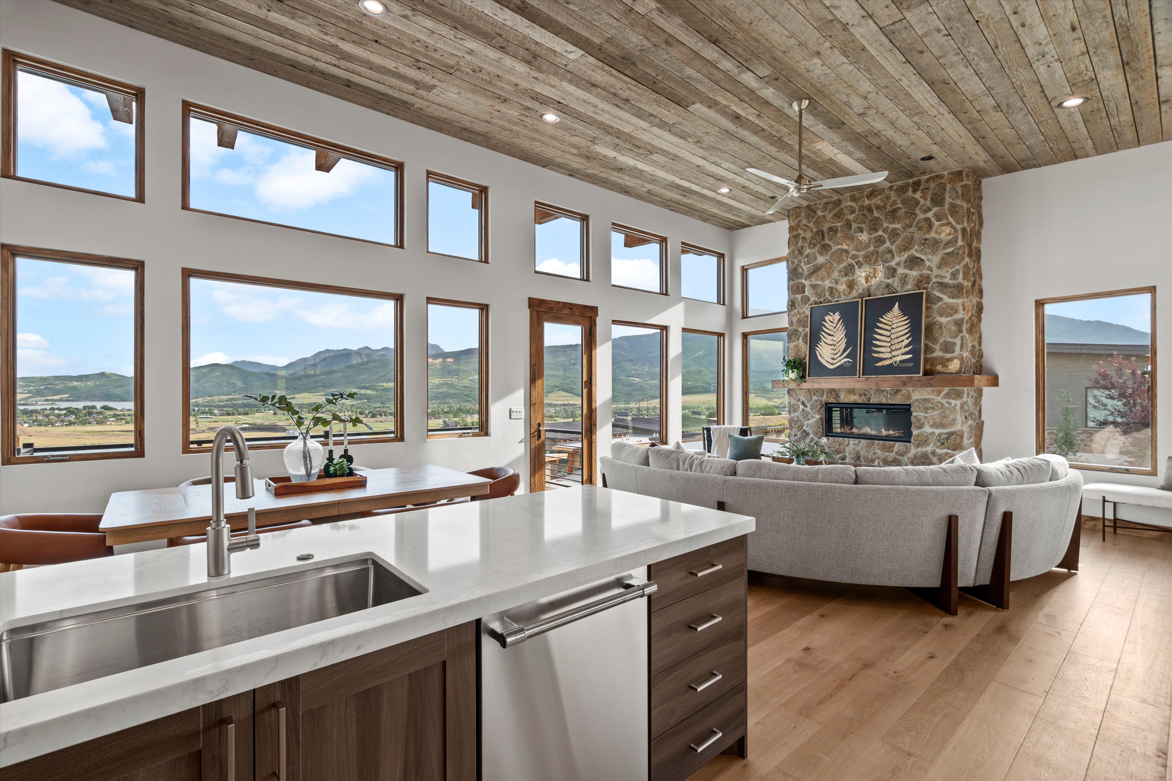 Open-concept living area with a stone fireplace, wood-finish flooring, and a natural wood plank ceiling