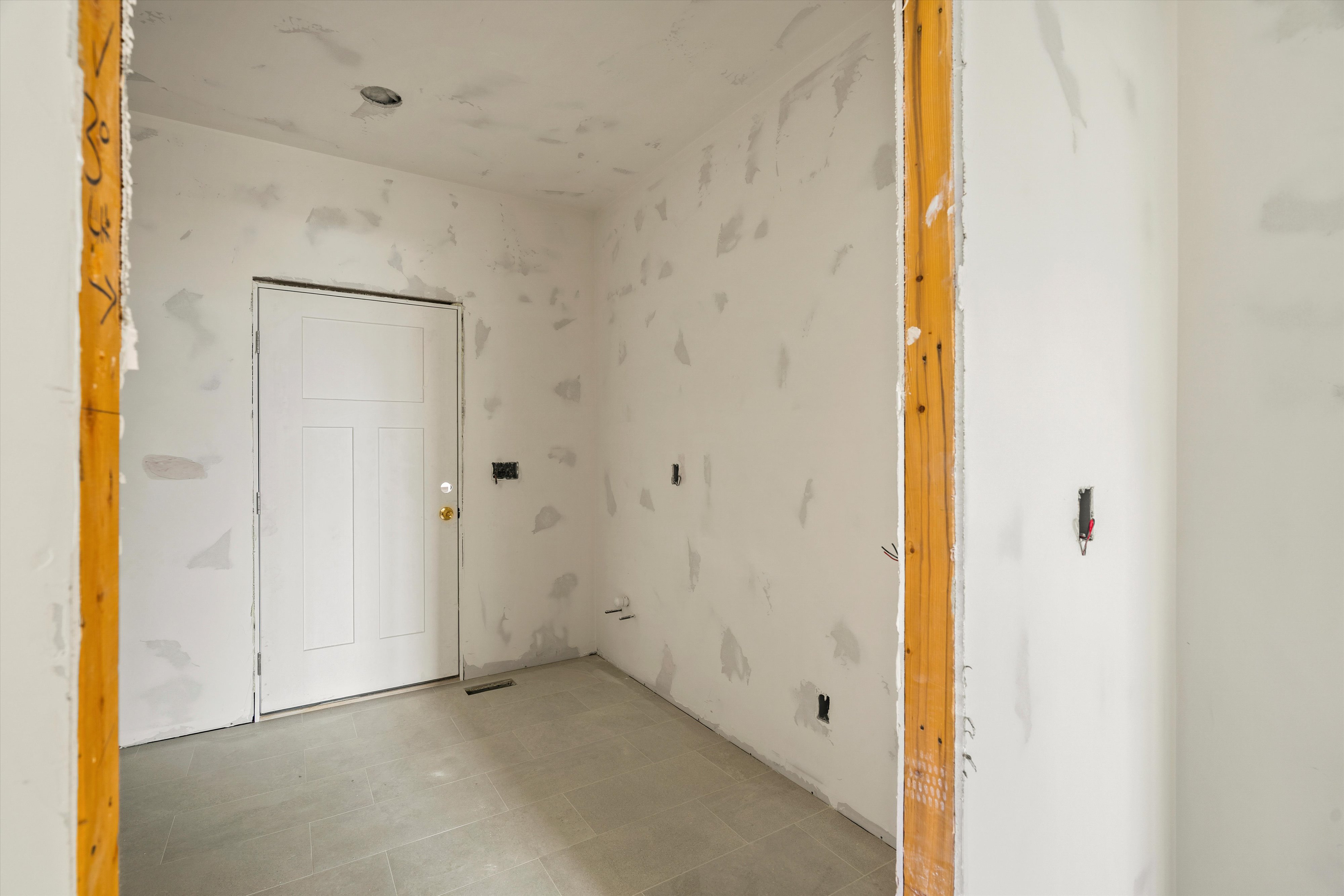 Interior space featuring gray tile flooring, a white paneled door with brass hardware, and recessed lighting