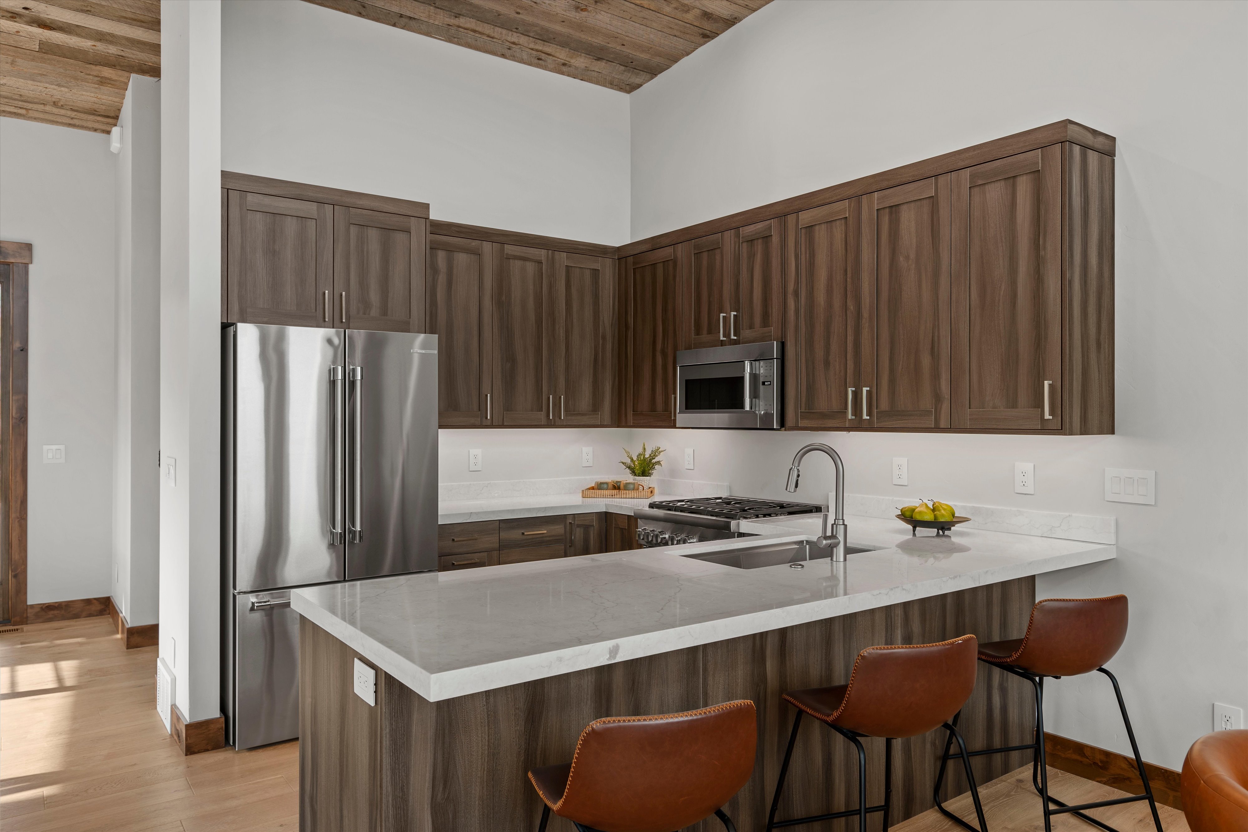 Kitchen featuring wood-finish cabinetry, stainless steel appliances, a center island with seating, light-toned countertops, and a wood-paneled vaulted ceiling