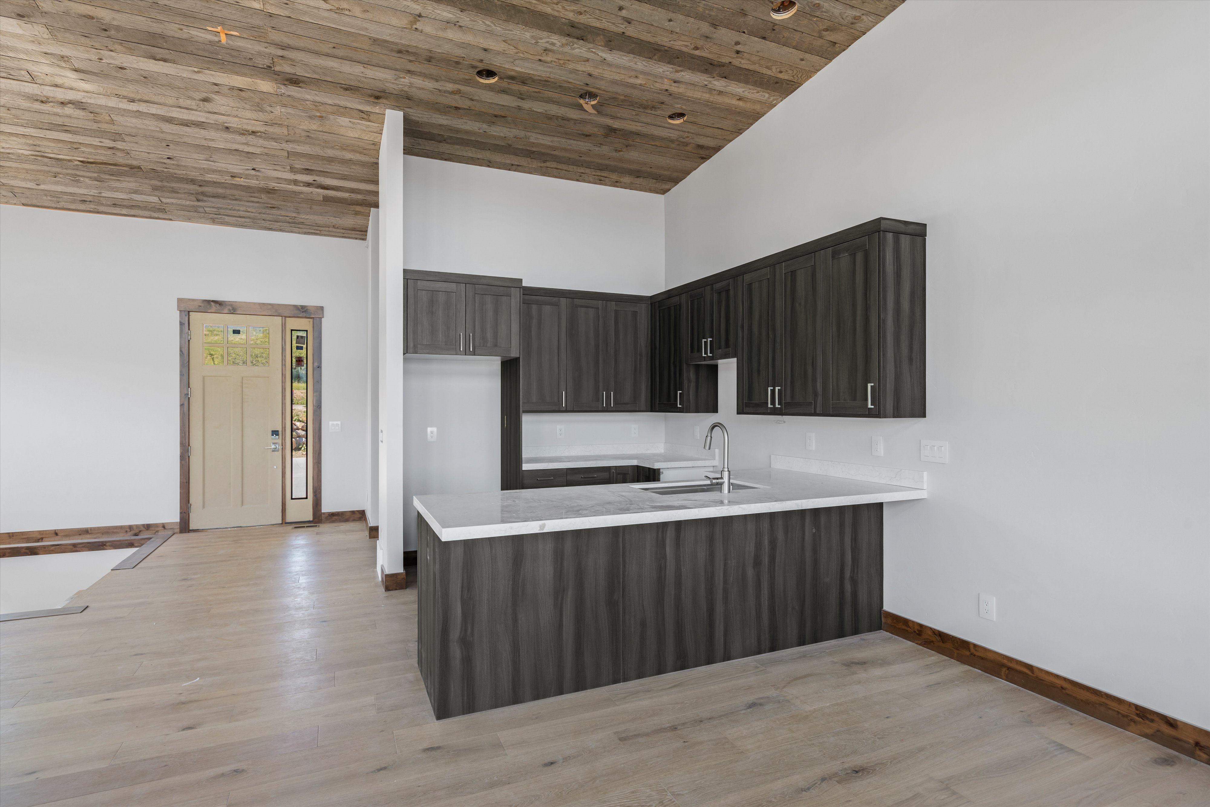 Modern kitchen area featuring dark wood-finish cabinetry, light countertops, and a stainless steel sink with a gooseneck faucet