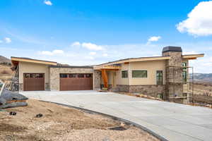 View of front of property featuring stone siding, concrete driveway, a garage, and a chimney