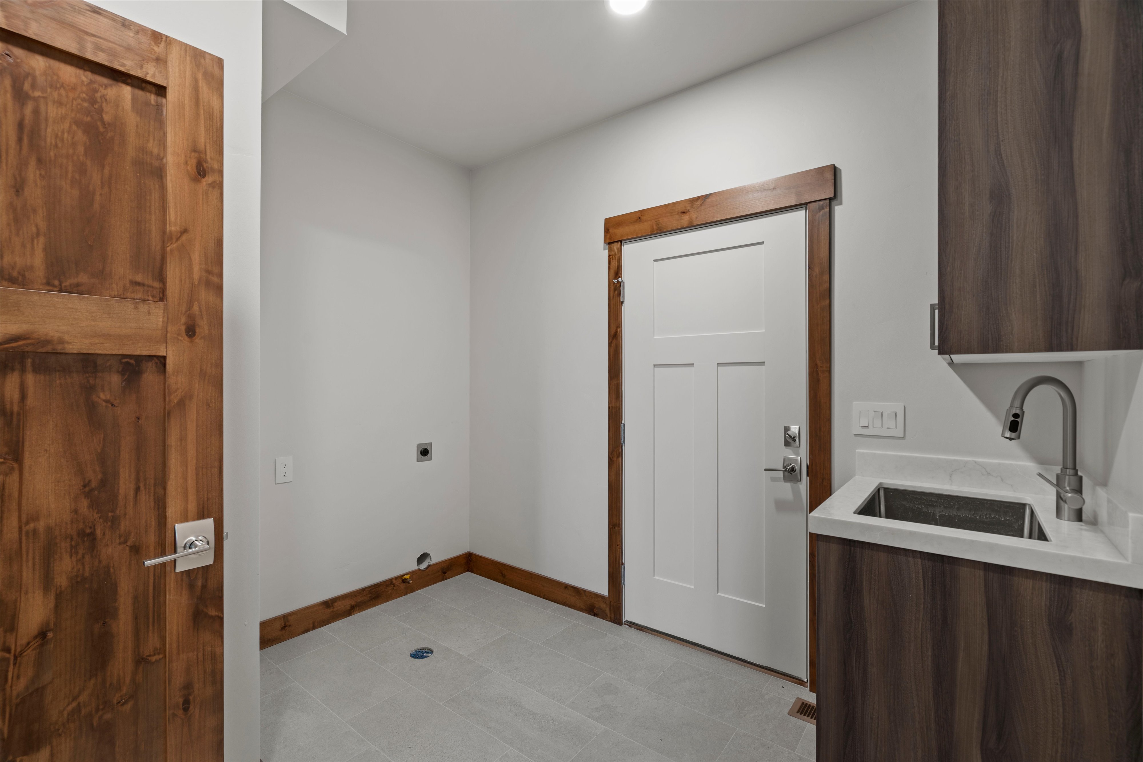 Utility room featuring a built-in sink with a gooseneck faucet, light-toned countertop, and dark wood-finish cabinetry