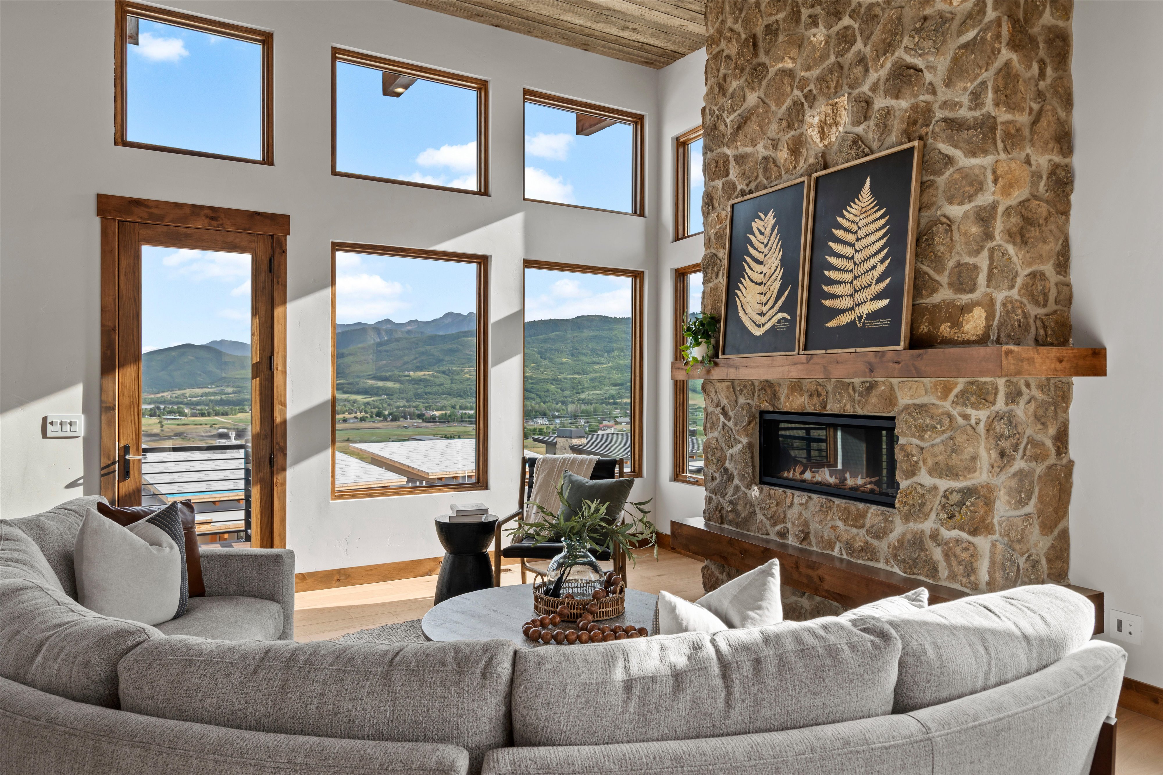 Spacious living area featuring a floor-to-ceiling stone fireplace with a wood mantel, a gas insert, and multiple large windows with natural wood trim