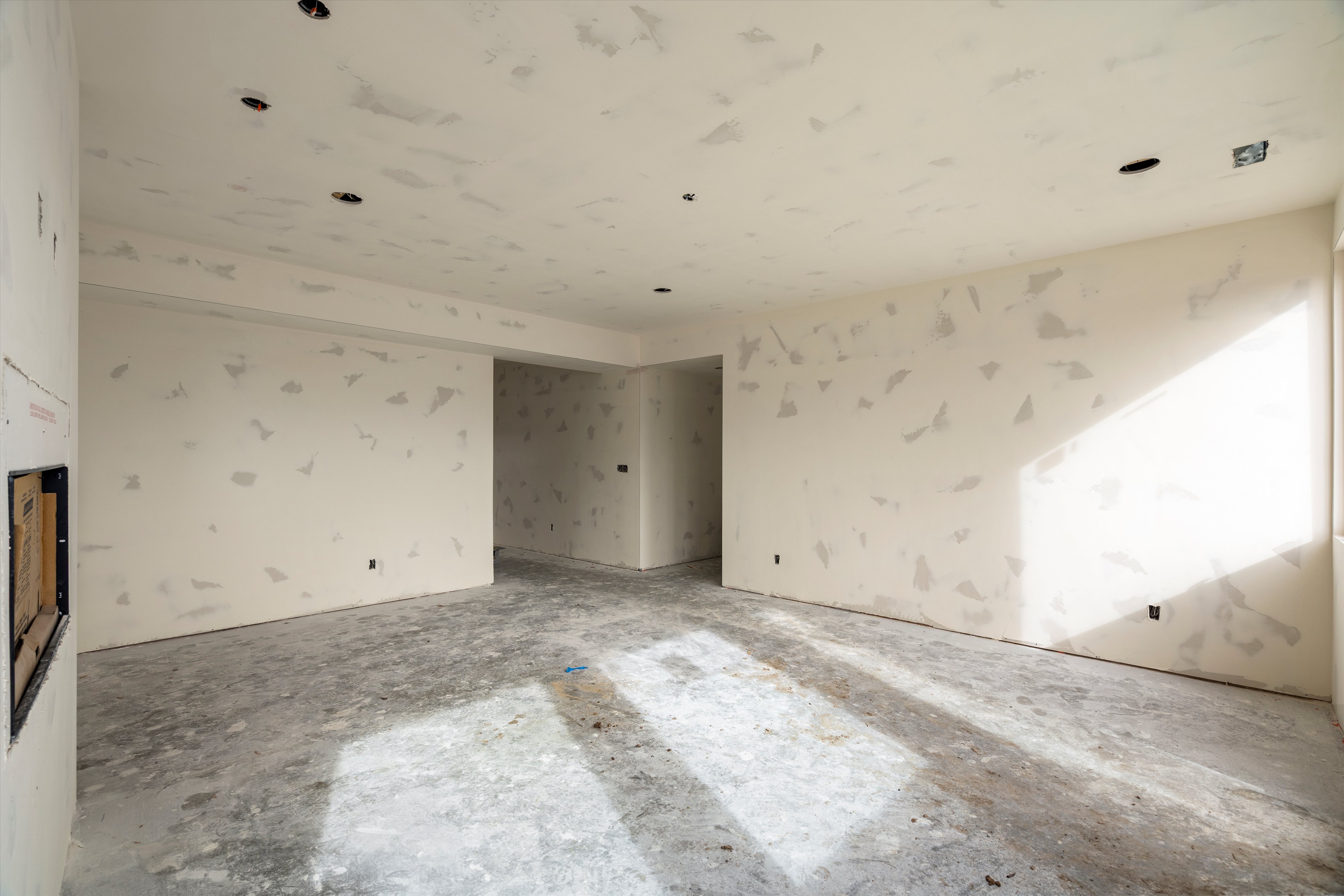 Unfinished interior space with neutral walls and exposed concrete flooring, featuring recessed ceiling lighting, a large window, and defined wall sections