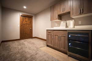 Bar area featuring wine cooler, recessed lighting, brown cabinetry, light wood-style floors, and light carpet