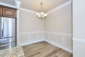 Unfurnished dining area featuring crown molding, light wood finished floors, a chandelier, wainscoting, and a decorative wall
