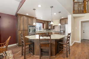 Kitchen with a kitchen island, decorative light fixtures, a breakfast bar, light stone countertops, and dark wood finished floors