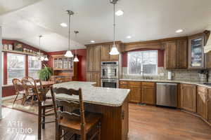 Kitchen featuring glass insert cabinets, tasteful backsplash, light wood-style floors, stainless steel appliances, and brown cabinets