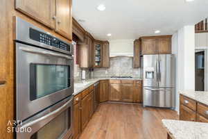 Kitchen with appliances with stainless steel finishes, dark wood-type flooring, light stone counters, brown cabinets, and recessed lighting