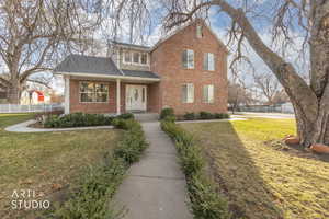Traditional home featuring brick siding, a shingled roof, and covered porch
