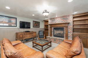 Living area featuring wainscoting, a brick fireplace, a textured ceiling, wood walls, and recessed lighting