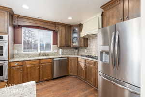 Kitchen with stainless steel appliances, light stone counters, dark wood-style flooring, brown cabinets, and decorative backsplash