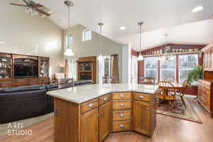 Kitchen featuring brown cabinetry, a kitchen island, light stone counters, hanging light fixtures, and open floor plan