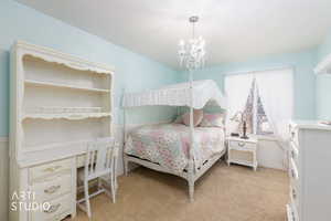 Bedroom featuring a chandelier, light colored carpet, a desk, and wainscoting