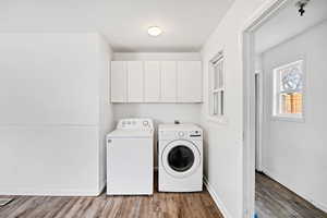 Laundry room with wood finished floors, cabinet space, and washing machine and dryer