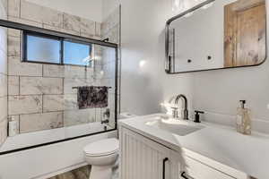 Bathroom featuring vanity, shower / bath combination with glass door, and dark wood-type flooring